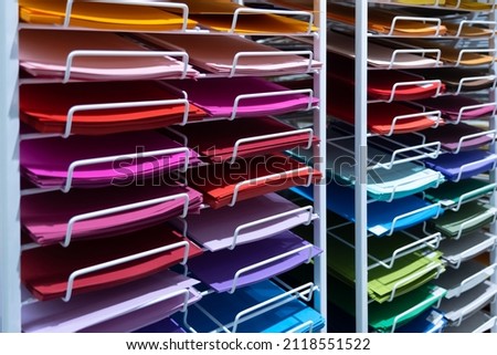 In the store, there are sheets of multi-colored paper on the racks. large selection of colors