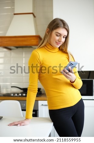 Happy blonde woman typing message on mobile phone. Beautiful young adult female with blond hair using modern smartphone for communication online on social media app while being at home on lockdown Royalty-Free Stock Photo #2118559955