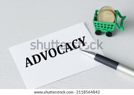 A white card with the text ADVOCACY on the table rippled pen and coins in the shopping cart