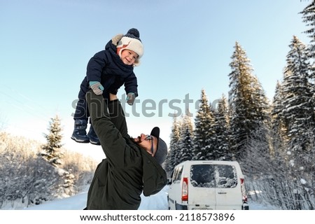 a father with a beard and glasses holds his little son in his arms on a winter walk against the backdrop of a snowy forest