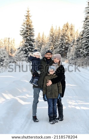 a portrait of a family standing in the snow where the father holds a small child in his arms and his wife and son stand next to him. the concept of a happy family in the snow.