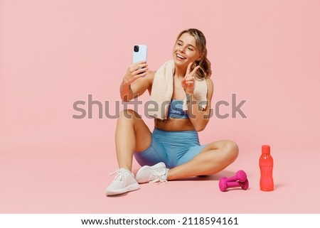 Full size young fitness trainer instructor woman wear blue tracksuit spend time in home gym do selfie on mobile cell phone show v-sign isolated on plain light pink background. Workout sport concept.