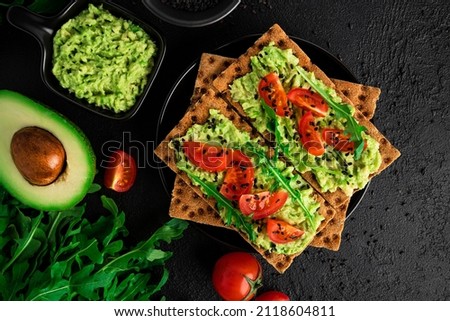 Avocado sandwich with avocado cream and rye crisp bread for snack. Fiber, fitness and diet food. Rye bread with guacamole, arugula and cherry tomatoes on dark background. High quality photo Royalty-Free Stock Photo #2118604811