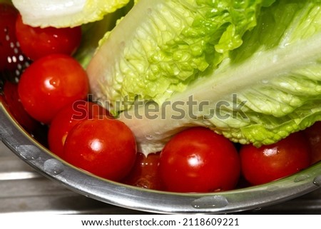 Close-up of small fresh tomatoes and lettuce leaves washed in a metal strainer. Tomatoes on the bottom in selective focus.