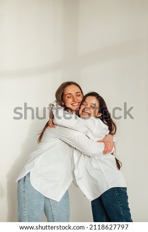 two girls in white shirts and jeans hugging on white background
