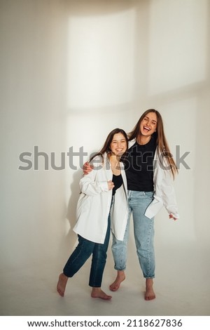 two beautiful girls in black T-shirts, white shirts and blue jeans standing together on white background