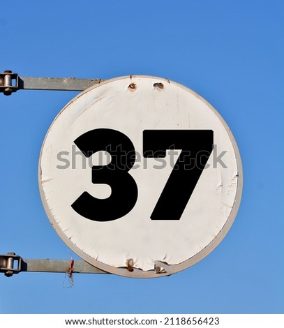 A round white sign, showing a black coloured number thirty seven (number 37) 