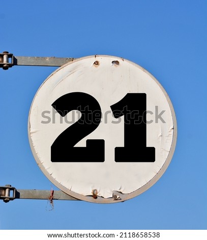 A round white sign, showing a black coloured number twenty one (number 21) 