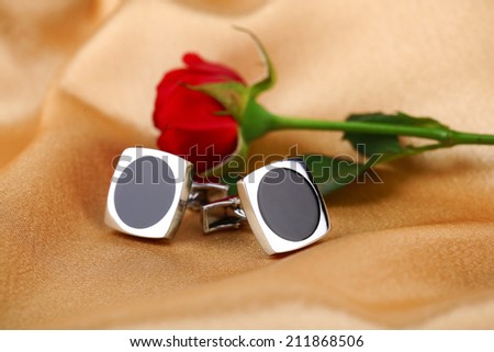 Pair of cuff links with red rose on light silk fabric background