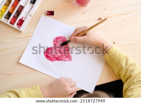 Boy in yellow clothes is making paper greeting postcard with hearts  for valentine day