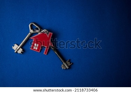 Key and house shaped keychain arrangement on blue background. Top view, flat lay. Real estate, insurance concept, mortgage, buy sell house, realtor concept Copy space
