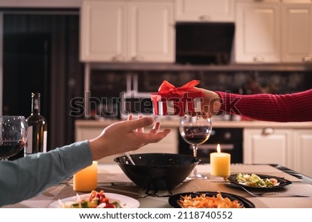 romance and gift of lovers at home in the kitchen, holding surprise gift with hands, dinner for two with wine and candles, couple no faces, valentine's day celebration concept Royalty-Free Stock Photo #2118740552