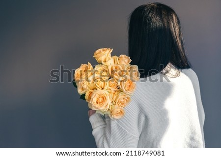 Woman with a bouquet of orange roses on a gray background.