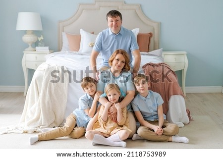 Family portrait caucasian parents with children are sitting on floor in bedroom. An attractive large family sitting on bed with adorable children early morning enjoying upbringing children in house.