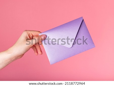 Hand holding purple envelope for Valentines day, gift certificates on pink background. High quality photo