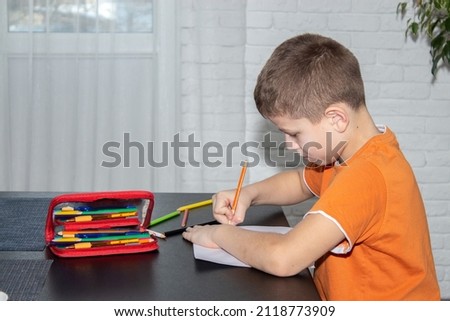 A boy of 7-10 years old draws with colored crayons at the table.
