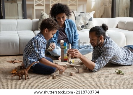 Happy caring loving young African American couple parents playing wooden toys with small cute multiethnic child son, enjoying creative playtime activity together in modern living room, childcare Royalty-Free Stock Photo #2118783734