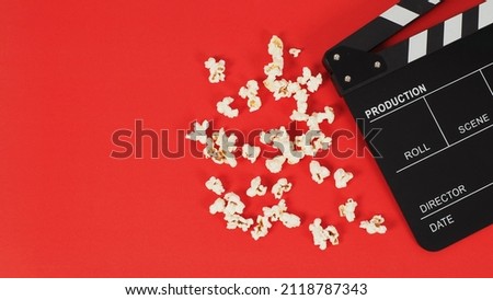 Black Clapper board or movie slate and popcorn on a red background.
