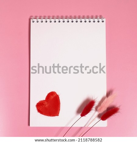 Empty notebook with a spring, a red textile heart and dried lagurus flowers on a pink background. Square format