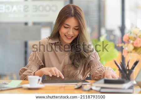 Attractive female freelance beauty blogger editing her picture for her online blog on digital tablet computer in coffee shop.