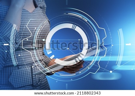 Businesswoman wearing formal dress is holding tablet device. Blue background. Digital interface with circle hologram in the foreground. Concept of modern technologies in contemporary business