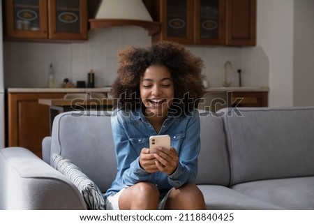 Cheerful happy gen Z teen girl receiving exciting message on smartphone, reading text in screen, smiling, laughing, sitting on couch, using online virtual app on mobile phone Royalty-Free Stock Photo #2118840425
