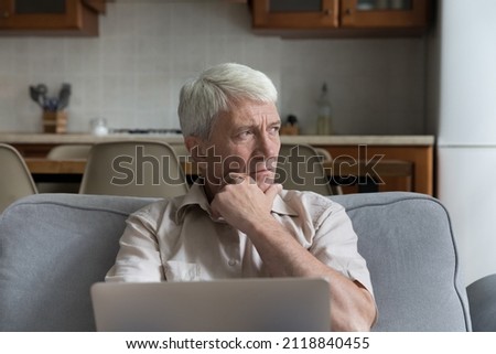 Pensive stressed mature 70s man holding laptop computer, looking away in deep sad thoughts, thinking over bad concerning news, health problems, sitting on home couch, feeling worried, frustrated Royalty-Free Stock Photo #2118840455