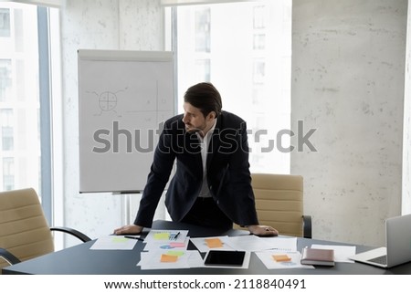 Frustrated concerned business man standing at table with sales reports, paper sticky notes, looking away, thinking over company future, negative statistics result, financial loss Royalty-Free Stock Photo #2118840491