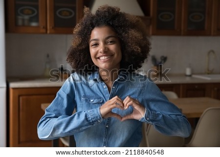 Happy excited teenage Black girl making hand heart shape. Cute teenage high schoolkid showing love, care, support sign, looking at camera, smiling. Youth, charity, donation concept. Head shot portrait