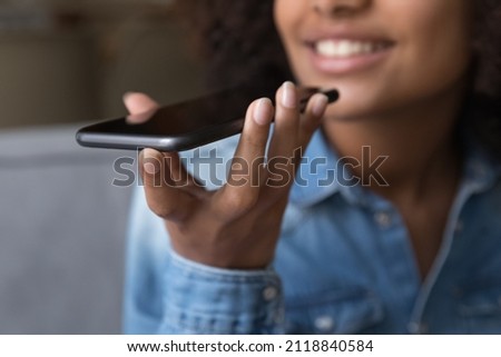 Happy teen African girl giving voice commands to virtual assistant on smartphone, speaking for recording audio message, holding, using mobile phone, smiling. Hand with cellphone close up Royalty-Free Stock Photo #2118840584
