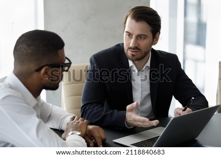 Serious boss, executive, business leader talking to African employee, discussing work on project, giving guidance, asking report. Serious professional, expert giving consultation to client Royalty-Free Stock Photo #2118840683