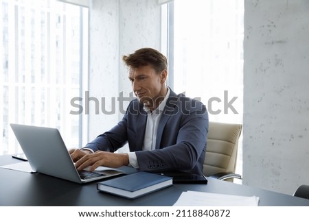 Serious busy middle aged businessman typing on laptop at workplace. Company leader, boss, CEO using online app, software on computer at table, working, chatting on internet Royalty-Free Stock Photo #2118840872