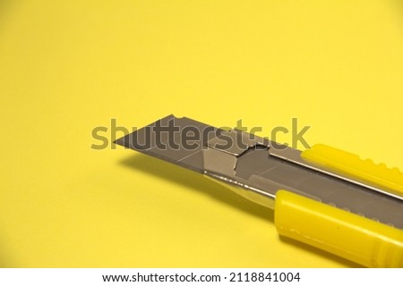 Stationery knife with blade. On a yellow background. Macro.