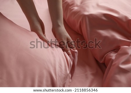 Woman making bed with beautiful pink silk linens, closeup view Royalty-Free Stock Photo #2118856346