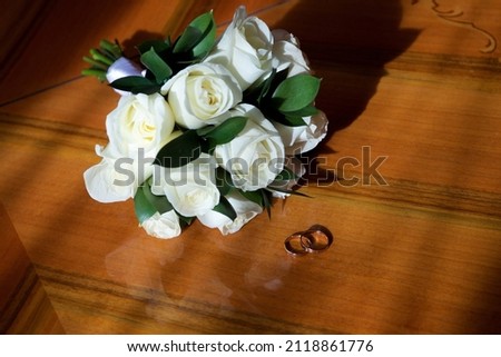 Обручальные кольца на деревянном столе на солнце рядом со свадебным букетом роз