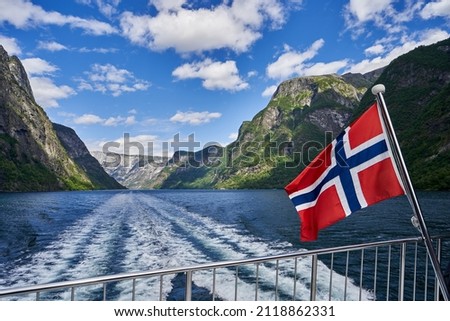 Cruise in Nærøyfjord, Norway. View of the fjord from the boat with Norwegian flag. Royalty-Free Stock Photo #2118862331