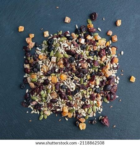 Mixed edible seeds and dried fruit (including sunflower, pumpkin linseeds, apricots and blueberries). Abstract, texture and pattern. Healthy vegetarian vegan food. Blue grey slate background. Flat lay