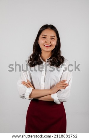 Portrait of a smiling young asian woman with red lipstick and crossed hands on a white background wearing a white shirt and a red pencil skirt