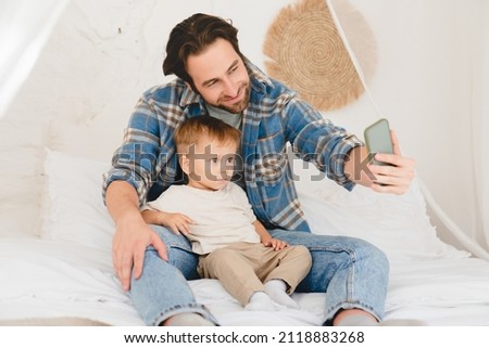 Young caucasian father dad taking selfie photo having videocall with small kid child toddler newborn infant baby at home on the bed. Videocall conversation online with relatives