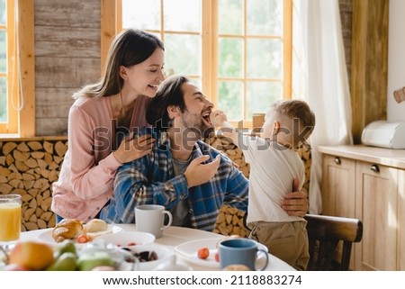 Funny family moments together. Morning breakfast with parents and little toddler kid child infant feeding father with cake at home kitchen. Parenthood and adoption Royalty-Free Stock Photo #2118883274