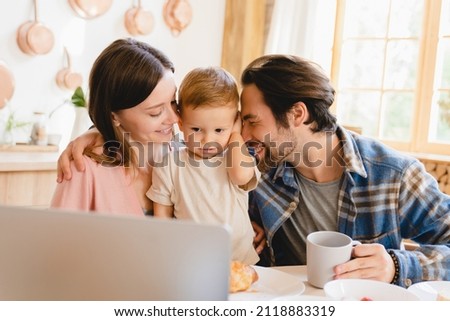 Happy family moments together. Caucasian young happy family nurturing taking care of small little kid child toddler infant baby at home kitchen, watching cartoons on laptop. Parenthood and adoption