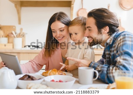 Child developing cartoons video. Caucasian happy parents watching animated movies, having videocall with grandparents on tablet with kid child toddler infant at home kitchen