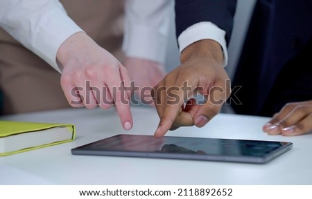 Hands of multiethnic people gathering around table and using tablet showing growth graph. Black man resizing screen with fingers, another person pointing with pen. Closeup of business meeting