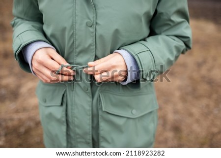 Close-up photo of woman in green trench, walking in the park.