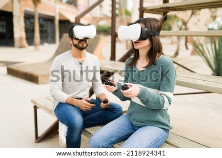 Young friends gaming outdoors. Attractive couple using VR glasses and playing a virtual reality video game 