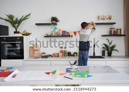 Boy decorating flat with garland from colored paper while preparing to the Fathers day Royalty-Free Stock Photo #2118944273