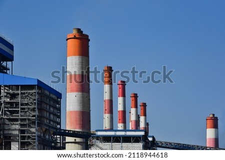 Coal power plant chimneys line up with coal conveyors and massive steel structures in the blue sky. Royalty-Free Stock Photo #2118944618