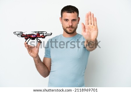 Young Brazilian man holding a drone isolated on white background making stop gesture