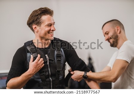 Personal trainer is helping a middle age man with dressing suit for EMS working out in the gym.