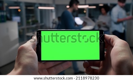 Pov shot of businessman using smartphone with blank green screen copy space in busy office. Employee holding cellphone working in coworking space 